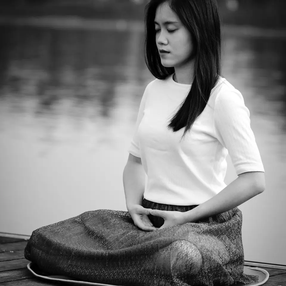 A woman meditating on a wooden jetty by a lake