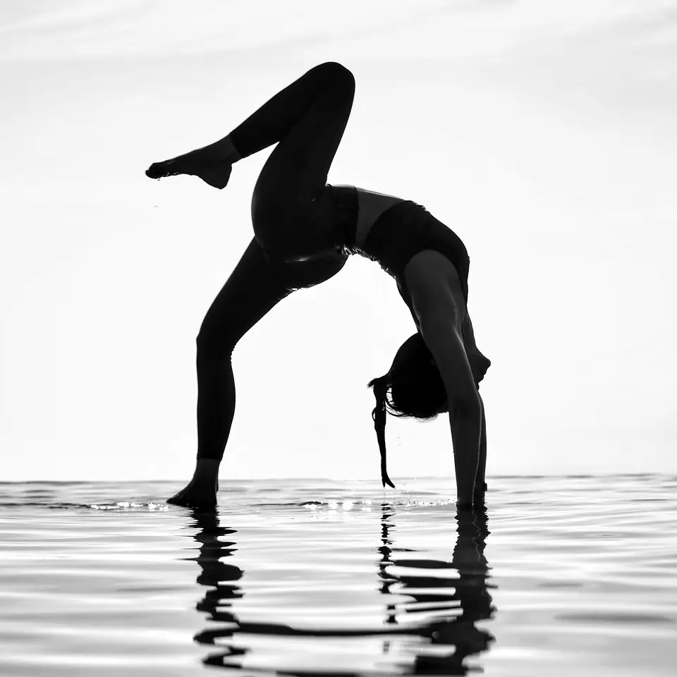 A woman holding a yoga backbend in shallow water at sunrise